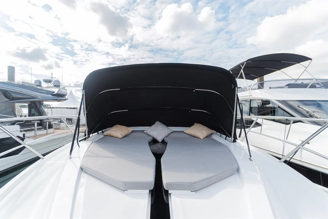 Luxury boat deck featuring two cushioned lounge areas with decorative pillows under a black canopy, surrounded by other boats.